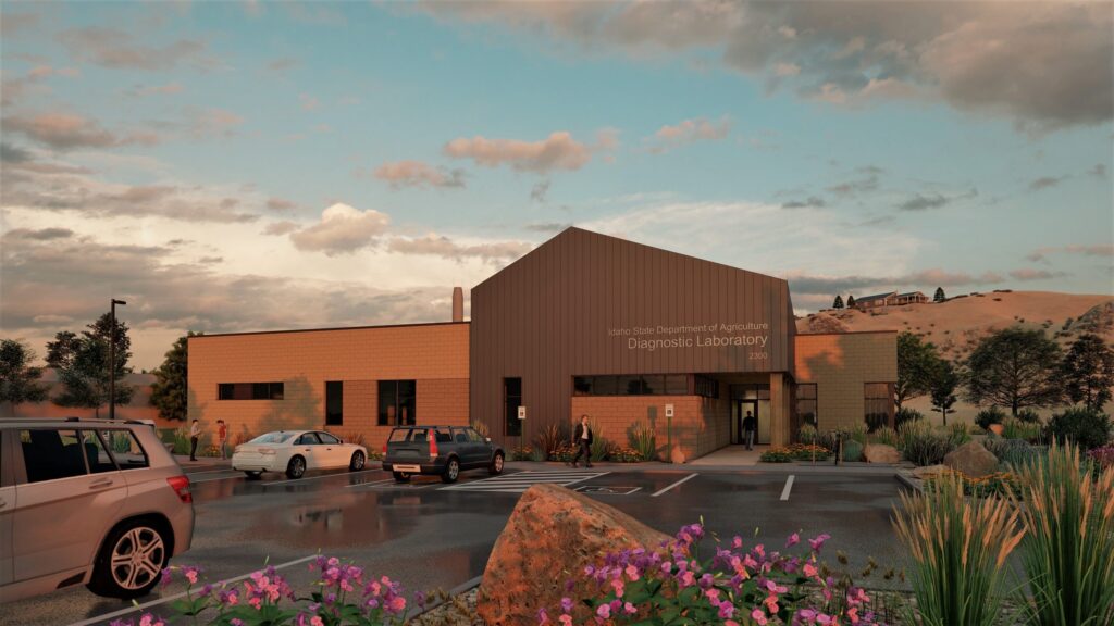 Modern building labeled "Idaho State Department of Agriculture Diagnostic Laboratory" surrounded by parking, cars, and plants under a cloudy sky, with distant hills.