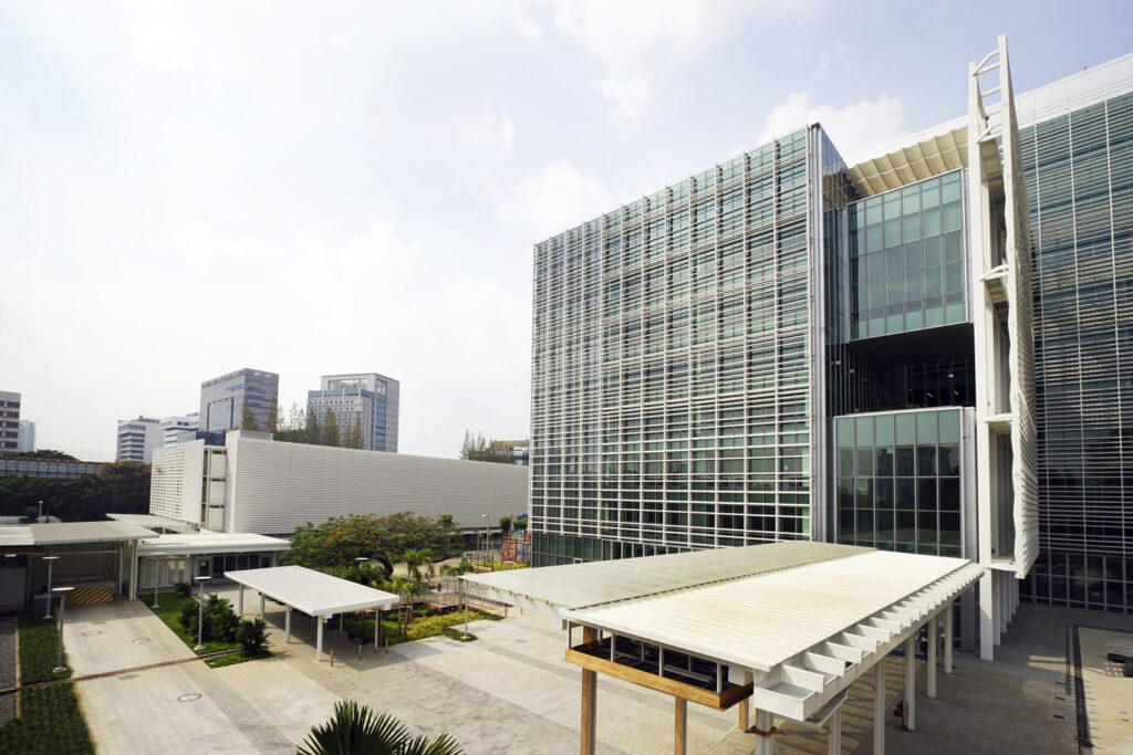 Modern architectural building with glass and steel facade, surrounded by greenery on a sunny day. Urban environment with a clear sky visible.