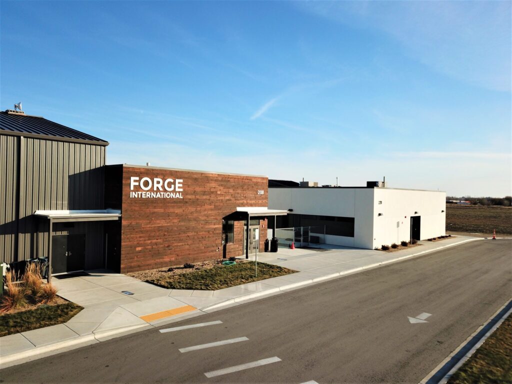 Modern building labeled "Forge International" on a sunny day, next to an empty road and open field, with a clear blue sky above.