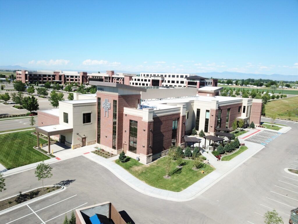 Aerial view of a modern brick-and-white church building with a large cross. Surrounding area includes trees, parking, and additional office structures.