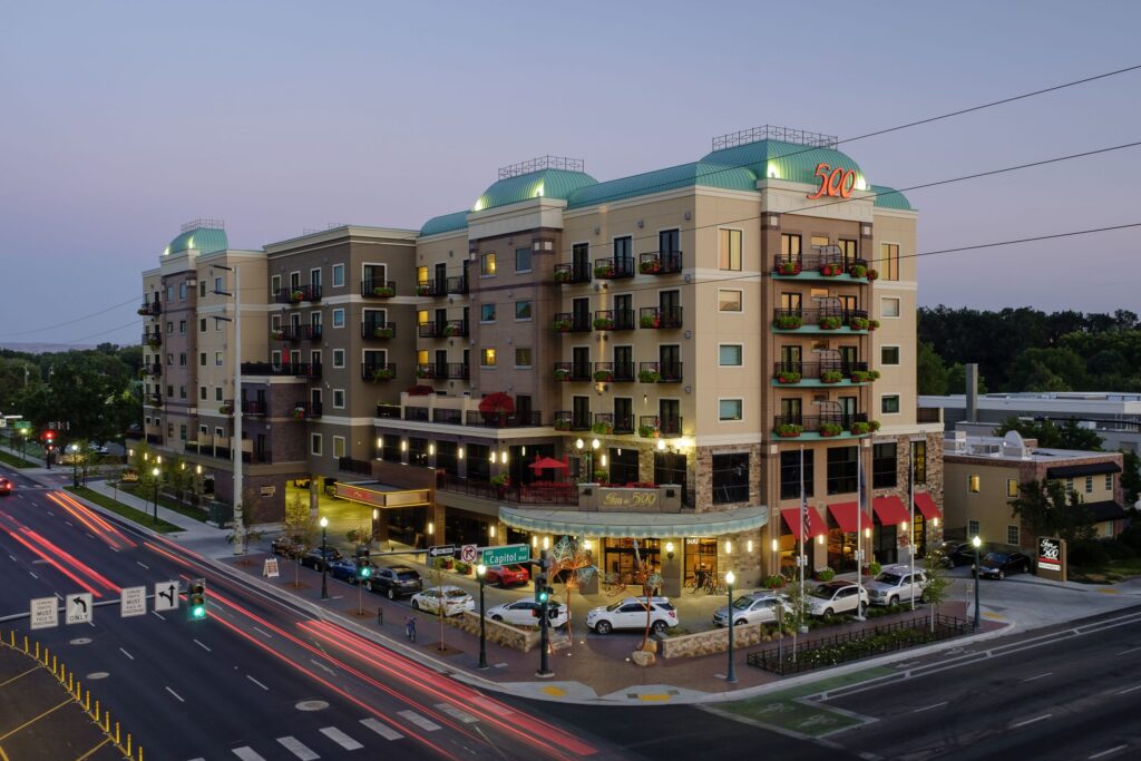 A multi-story building, identified as "Inn at 500," is illuminated at dusk. Cars and people are visible on the surrounding streets and sidewalks.