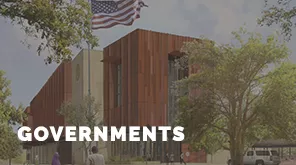 A person walks near a modern building with an American flag, surrounded by trees. The word "GOVERNMENTS" is displayed prominently.