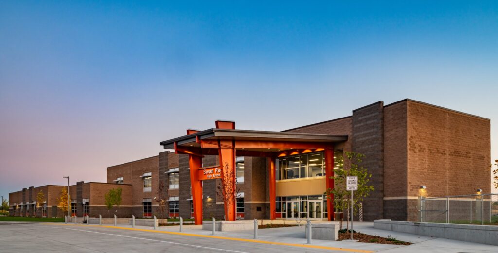 A modern brick building with large windows and an entrance sign reading "Swan Falls High School," under a clear dusk sky.